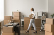© fizkes - Successful grey haired entrepreneur woman working on Internet store business, walking in storage room with stacked boxes, carrying cardboard packages, looking at camera, smiling. Full length shot