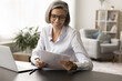 © fizkes - Positive senior entrepreneur lady in elegant eyeglasses reading legal financial paper document at home office workplace, smiling. Mature business woman satisfied with agreement terms