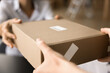 © fizkes - Female hands of transportation manager, courier, giving cardboard paper box to customer. Client getting parcel in Internet store storage, delivery service, post office. Cropped shot close up