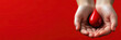 © iri.madrid.art - World hemophilia day awareness concept - hands holding blood drop symbol on a red background. Horizontal banner. Copy space. Blood donor awareness day