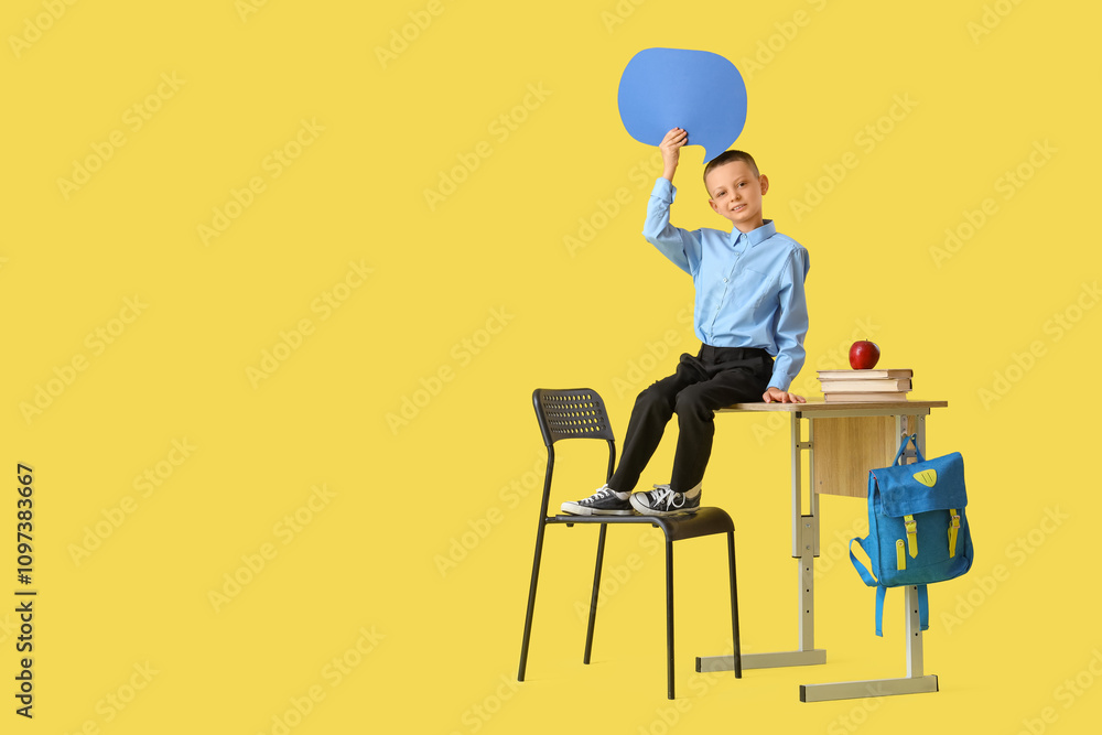Little schoolboy with blank speech bubble sitting on desk against yellow background