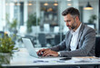 © Pixel Focus AI - A professional man in a gray suit is focused on his laptop in a bright, modern office. The workspace is clean, with a calm atmosphere, emphasizing productivity and successful business endeavors.