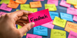 © Taskmanager - A hand holding a bright pink sticky note labeled 'Feedback,' with a vibrant background of colorful sticky notes representing collaboration, communication, and creative input