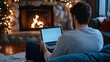 © Jiraphat - A cozy scene of a person sitting in front of a fireplace, using a laptop, surrounded by festive decorations and warm lighting.