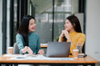 © Satori Studio - Two women enjoying a conversation in a cafe, surrounded by modern decor, with a laptop and coffee cups on the table.