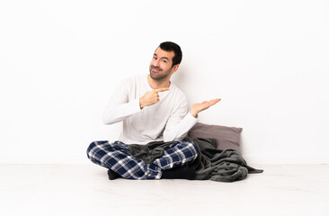 caucasian man in pajamas sitting on the floor at indoors holding copyspace imaginary on the palm to 
