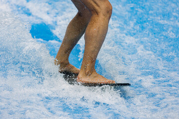 A male surfer makes big splashes while surfing a blue wave in a surf pool that is perfect for a surf simulator.