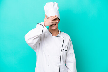 Wall Mural - Young caucasian chef woman isolated on blue background covering eyes by hands and smiling