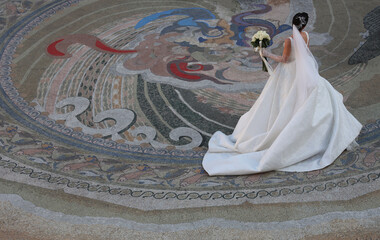 back rear view of georgian bride dancing alone with bouquet of flowers on mosaic floor of Piazza square background. Dressed in long white dress beautiful brunette lady. Top view. Batumi Georgia