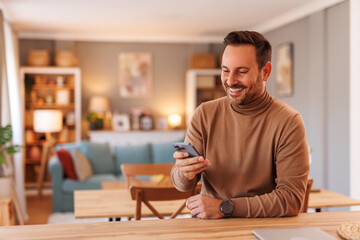 Wall Mural - Portrait of handsome freelancer smiling and texting over mobile phone while working in home office