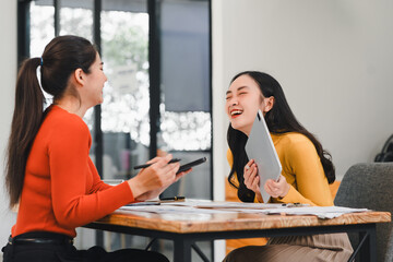 Wall Mural - Two women laughing and enjoying productive meeting at modern office table, sharing ideas and collaborating with enthusiasm