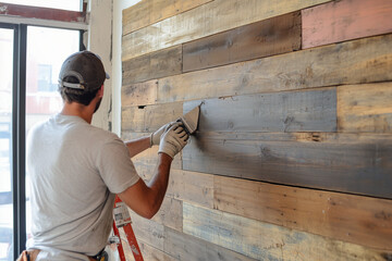 An experienced contractor refinishing a reclaimed wood accent wall in an urban loft, blending industrial decor with rich, natural tones for a modern yet cozy look.