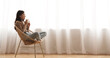 © Prostock-studio - Time to relax. Girl drinking coffee, sitting in wicker chair against window at home, free space