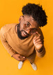© Prostock-studio - Excited young african man in glasses looking at camera, full body over orange background, top view