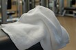 © Hafiz - Blank white gym towel on equipment with microfiber texture visible, captured using wide-angle lens on gym lighting, with copy space