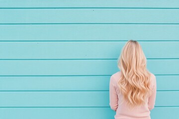 Wall Mural - Woman with long blonde hair standing against a bright blue wall in a relaxed pose