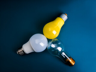 Wall Mural - Three type of electric light bulbs, clear, yellow and white, turn the bulbs towards each other, isolated on blue background. Brainstorm, creative and idea, business and technology, teamwork concept.