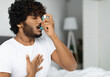 © Prostock-studio - Indian guy suffering from asthma, using inhaler in bed, side view, copy space. Young hindu man woke up with asthma attack, touching chest and using nebulizer, bedroom interior