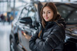 © S photographer - Young Caucasian woman poses with a new SUV in a car showroom.