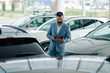 © Zamrznuti tonovi - Salesman in blue suit using tablet in a car dealership showroom.