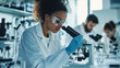 © Tanuha - Scientist in a lab coat and safety glasses examines samples under a microscope in a modern lab.