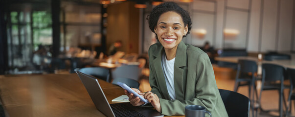 Wall Mural - A woman in a suit smiles at her laptop and phone on the table