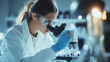 © Tanuha - Scientist in a lab coat and safety glasses examines samples under a microscope in a modern lab.