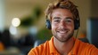 © Seyyar - Cheerful male customer support representative with headset wearing an orange shirt, smiling warmly in a bright office environment.