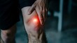 © Sam - Close-up of a male hand gently pressing a knee showing indications of pain with a glowing red spot.