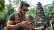© pisan thailand - A traveler checks his phone while exploring ancient ruins surrounded by lush greenery, wearing sunglasses and a backpack.