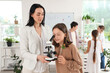 © Pixel-Shot - Teenage girl with plant looking through microscope and teacher in Biology class