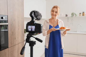 Wall Mural - Mature woman with tasty pasta recording cooking video class in kitchen