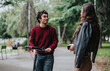 © qunica.com - A young man and woman interact casually in a park, sharing a moment of friendly conversation. The setting is relaxed and natural, surrounded by greenery.