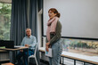 © qunica.com - A student speaks confidently in a classroom as an elderly professor watches attentively, fostering a supportive learning environment.