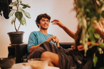 Wall Mural - A joyful young couple enjoys a relaxed moment together in a cozy home environment, surrounded by plants and warm decor.