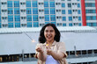 © M Alfan Setyawan - carefree asian young woman holding sparkler celebrate new year eve with laugh and dance in rooftop apartment outdoor with city building background