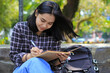 © M Alfan Setyawan - smiling asian beautiful young woman enjoy writing to do list and idea in notebook in outdoors city park