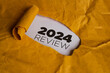 © Jamaludinyusup - A yellow piece of paper with a hole torn in it. Through the hole, a white piece of paper is visible with the text '2024 REVIEW' written in black. This represents the concept of reviewing the year 2024