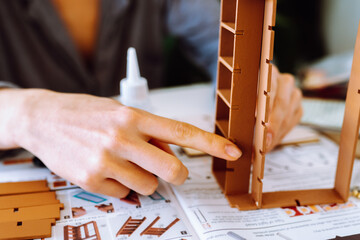 Wall Mural - female hands assembling wooden architectural model using glue in bright room