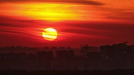 Wall Mural - Sunset over a cityscape with the sun setting behind buildings. Urban skyline silhouette with red and orange sky