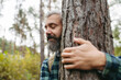 © Halfpoint - Handsome man standing in forest with closed eyes, hugging tree. Peaceful atmosphere of the nature, forestbathing.