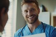 © ttonaorh - Close-up of a handsome male doctor wearing blue scrubs, smiling while showing medical notes to a patient in his office