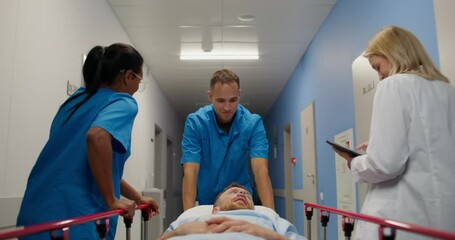 Wall Mural - Medical workers carry a patient on a gurney along the hospital corridor. They are smiling and talking to a man