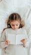 © ArtCookStudio - Young girl reading a book while lying on a cozy white blanket indoors
