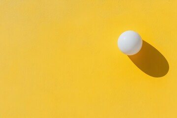 Poster - White ball casting a shadow on a bright yellow background in a minimalist setting