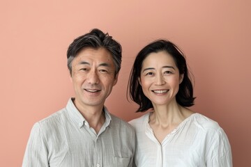 Wall Mural - Portrait of a grinning asian couple in their 40s wearing a simple cotton shirt while standing against solid pastel color wall