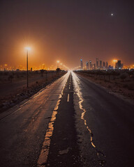 Poster - Road with a city in the background. The road is wet and the street lights are on