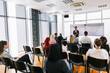 © Mediteraneo - African American woman CEO standing in front of a multiracial group of colleagues. Multimedia classroom with smart board and graphics on them.