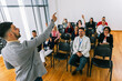 © Mediteraneo - Male CEO standing in front of a multiracial group of colleagues and calls out someone to answer the question. Multimedia classroom with smart board.