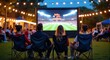 © MarGa - A group of friends sits in folding chairs watching a large outdoor screen displaying a live football game under string lights, creating a cozy atmosphere for tailgating parties or movie nights